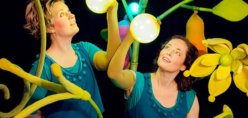 Turkosklädda skådespelerskor med gula ljusbollar i handen