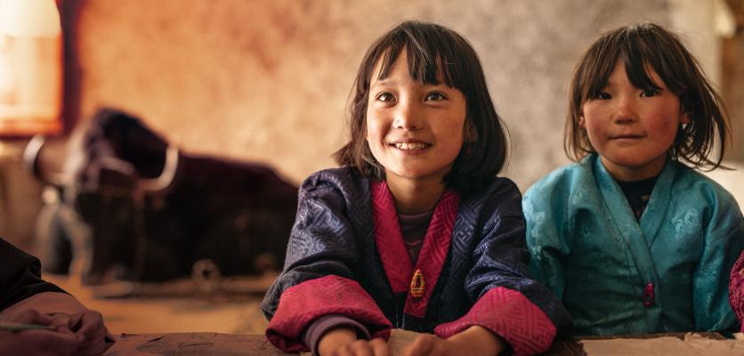 Två små barn i färgglada kläder i Bhutan med en Takin i bakgrunden