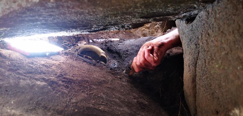En hand gräver i jorden upplyst av en ficklampa