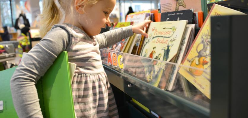 En 4-åring väljer bilderböcker ur de mörkgröna boktrågen på Alingsås biblioteks barnavdelning